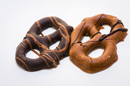 A grouping of two pretzels coated with dark and light chocolate on a white background.