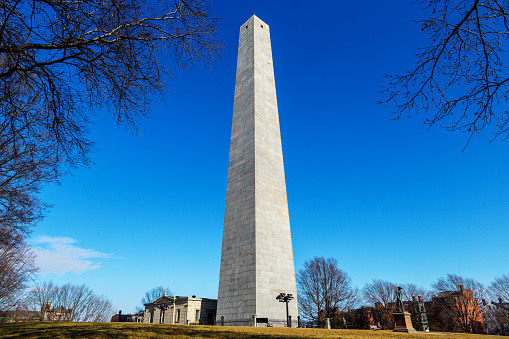 Boston, Massachusetts, USA - February 15, 2023: The Bunker Hill Monument is a monument erected at the site of the Battle of Bunker Hill in Boston, which was among the first major battles between the Red Coats and Patriots in the American Revolutionary War. The granite obelisk was erected between 1825 and 1843 in Charlestown, Massachusetts.  In front of the obelisk is a statue of Colonel William H. Prescott, a hero of Bunker Hill. According to popular stories, he coined the famous Revolutionary War phrase \