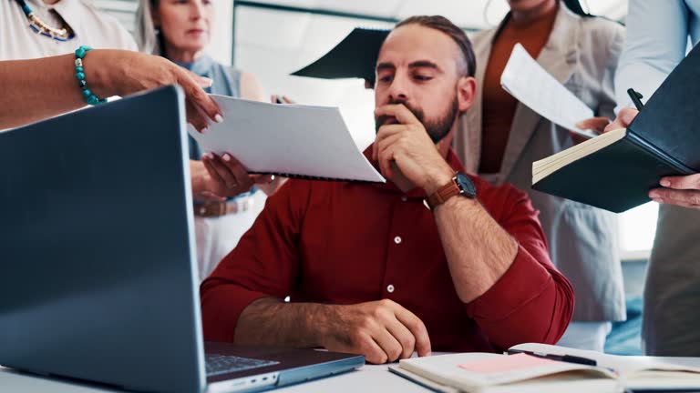 Business man, multitasking and stress with chaos and overworked boss, mental health and frustrated in workplace. Tired businessman at desk, laptop and paperwork with team and overwhelmed with burnout