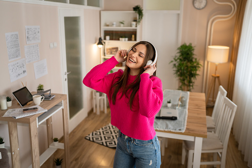 One woman young caucasian female teenager dancing alone at home with headphones on her head having fun while listen to the music happy smile real people copy space