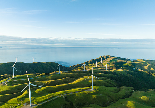 Majestic view of beautiful green hills with wind turbines on them and sea coast as background.