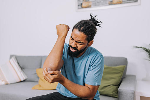 A mid-adult African-American man is sitting and holding his painful elbow.