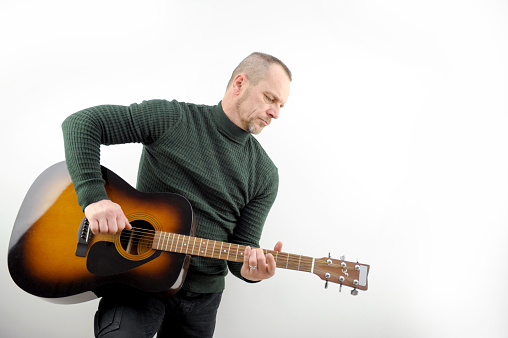 Music melody under the verses adult confident man playing the guitar on white background in the studio green sweater golf under the neck beard and mustache jeans