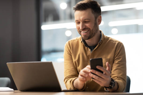 istock Happy Entrepreneur Man Texting Using Smartphone Near Laptop In Office 1466839603