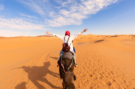 istock A tourist girl with a traditional moroccan red dress, open arms, riding a dromedary in the Sahara desert of Merzouga, Morocco 1466845276