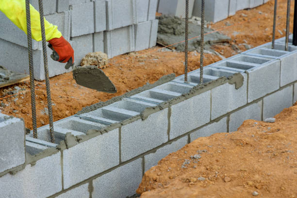 um pedreiro, um pedreiro, está colocando a montagem de uma parede de blocos de concreto que serão usados como parte de um projeto de construção. - mason brick bricklayer installing - fotografias e filmes do acervo