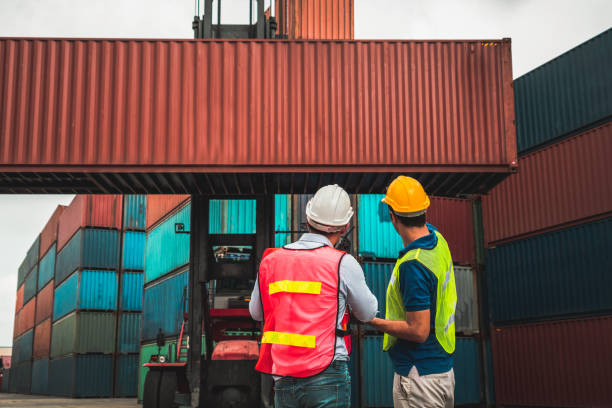 istock Industrial worker works with co-worker at overseas shipping container yard . Logistics supply chain management and international goods export concept . 1466851586