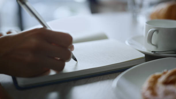 istock Woman hand taking notes writing pen notebook at remote workplace cafe table. 1466855649