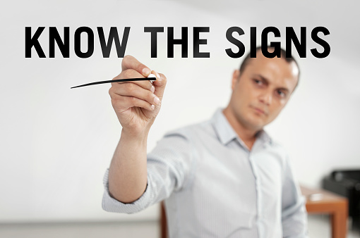 Businessman writing “Know the signs” on a transparent wipe board