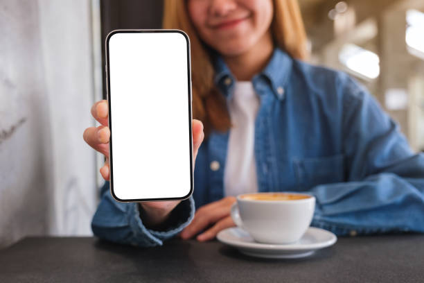 istock Mockup image of a woman holding and showing a mobile phone with blank white screen while drinking coffee in cafe 1466862801