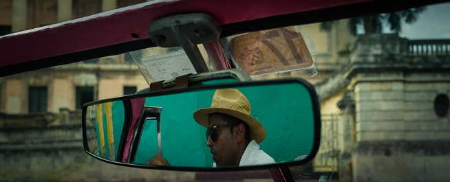 Driver of a vintage convertible car on a green background shot from the rear view mirror in old town of Havana Cuba.