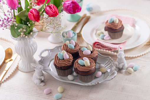 Homemade easter chocolate cupcakes bird's nest with chocolate cream and candy eggs on a dish.