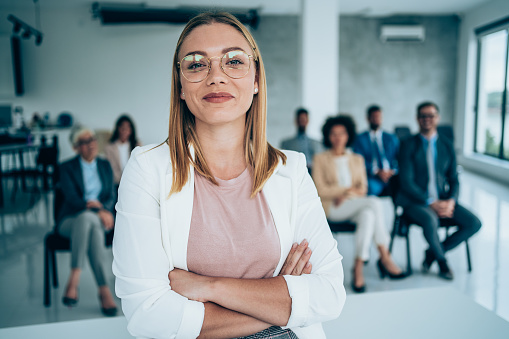 Shot of confident business leader standing in a board room with crossed arms and looking at camera. Businesswoman leading a training class for professionals.