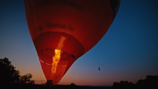Bright propane flame inflating hot air balloon in dark field at dawn