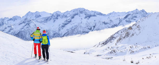 파노라마 겨울 스포츠 커플 알파인 스키. 여자와 남자 스노우 스키어가 스키 리조트에서 포옹하고 있다. 파우더 스노우. 높은 산의 눈 덮인 풍경.  알프스 산맥 유럽 - romance skiing ski resort couple 뉴스 사진 이미지