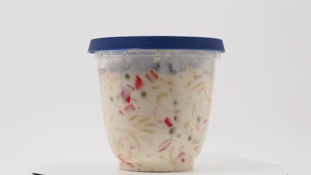 Vegetarian pasta salad in a plastic jar on a white background.