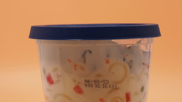 Vegetarian pasta salad in a plastic jar on an orange background.