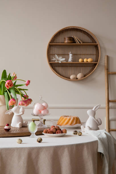 istock Interior design of easter dining room interior with round table, shelf on wall, colorful eggs, easter cake, hare sculptures, vase with tulips, lychee and personal accessories. Home decor. Template. 1466936455