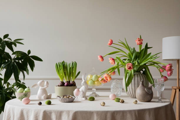 design intérieur de la salle à manger de pâques avec œufs colorés, sculptures de lièvre blanc, vase avec tulipes, plantes, lampe, mur beige avec stuc, poule grise et accessoires personnels. décoration intérieure. modèle. - showcase interior home decorating architecture home interior photos et images de collection