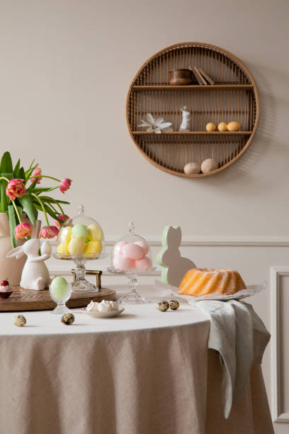 istock Interior design of easter dining room interior with round table, shelf on wall, colorful eggs, easter cake, hare sculptures, vase with tulips and personal accessories. Home decor. Template. 1466936687