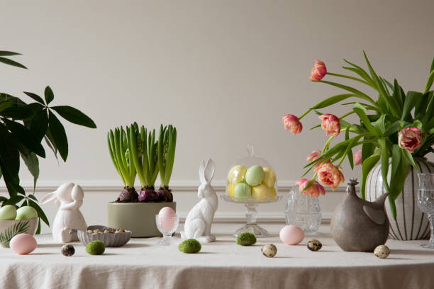 inneneinrichtung des osterspeisesaals mit bunten ostereiern, weißen hasenskulpturen, vase mit tulpen, pflanzen, lampe, beige wand mit stuck, grauer henne und persönlichen accessoires. wohnkultur. schablone. - showcase interior home decorating architecture home interior stock-fotos und bilder