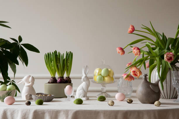 interior design of easter dining room with colorful easter eggs, white hare sculptures, vase with tulips, plants, lamp, beige wall with stucco, gray hen and personal accessories. home decor. template. - easter easter egg eggs spring imagens e fotografias de stock