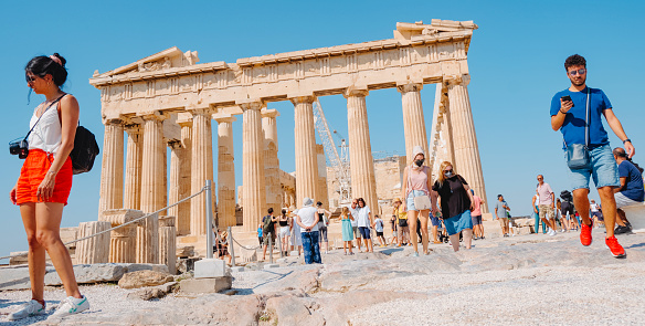 Athens, Greece - August 30, 2022: A crowd of people are visiting  the Acropolis of Athens, in Greece, in front of the remains of the famous Parthenon