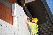 A construction worker insulates a building with styrofoam. Installation of polystyrene on the facade of the building.