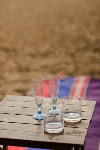 A vertical shot of empty drinking glasses on a wooden table in the middle of a desert field