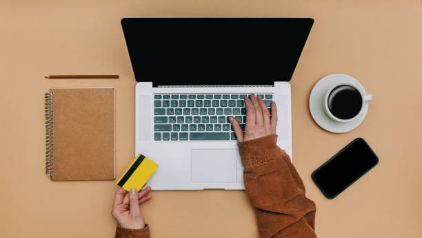 istock Top view on female customer hands with card and laptop computer next to notebook, mobile phone and cup of coffee while purchase 1466944454
