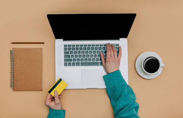 istock Top view on female customer hands with card and laptop computer next to notebook and cup of coffee while pur 1466944475