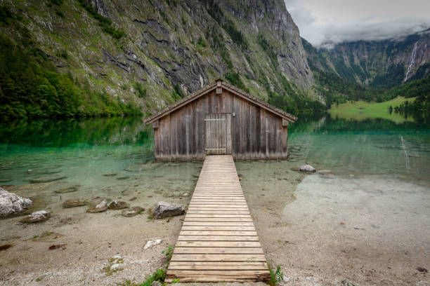 Panoramic view traditional old wooden boat house at scenic Lake Obersee on a beautiful day with blue sky and clouds in summer, Bavaria, Germany
