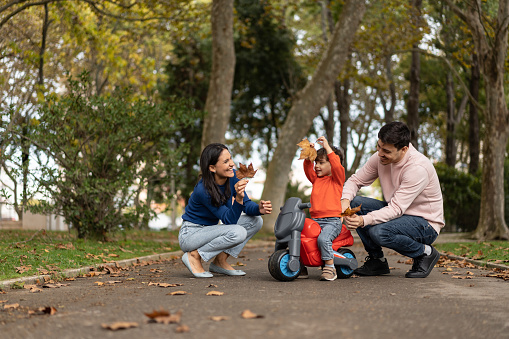 Happy family playing with leaves in public park in autumn