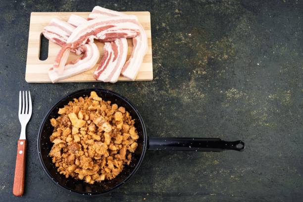 a pan with some bacon and onions on a table near a knife and fork