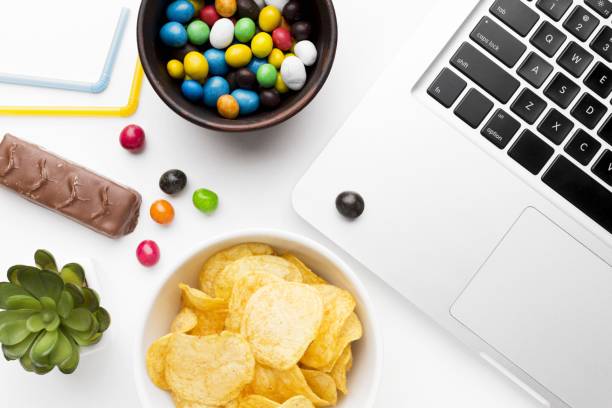 laptop keyboard, a chocolate bar with bowls of candies and chips on a white background - choc chip imagens e fotografias de stock