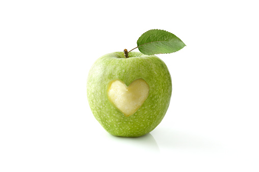 Green apple eaten in the center with a heart shape reflected on white table and isolated background. Front view.