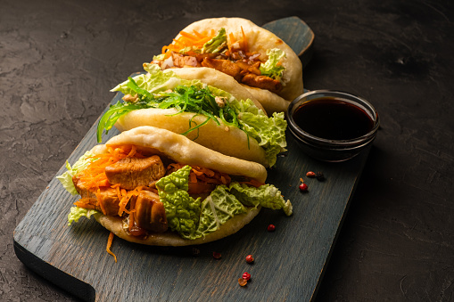Steamed bao buns with chicken and vegetables on a dark background.