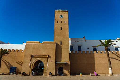 Morocco. Essaouira. People walking along the ramparts and the Magana clock tower