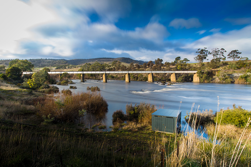 A railway bridge in the countryside of Tasmania, over a blue lake on a cloudy day