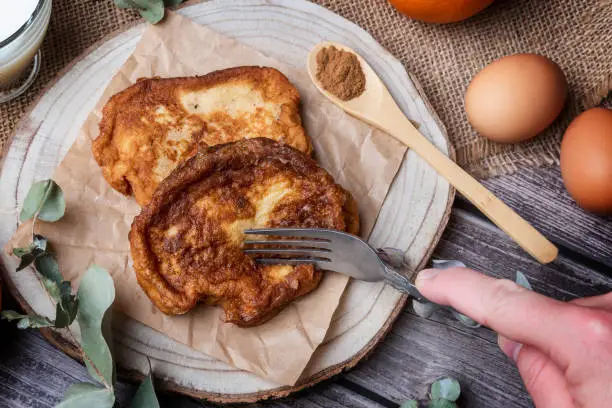 Photo of Torrijas. Hand with a fork cutting the typical Spanish sweet made of bread, milk, eggs, sugar, cinnamon and orange zest that is consumed during Carnival and Easter