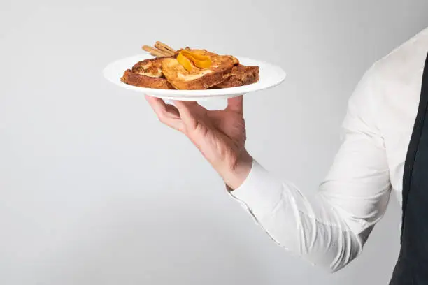 Photo of The hand of a waiter lifting a plate of gourmet torrijas. A typical Spanish sweet made with bread, milk, eggs, sugar and cinnamon that is consumed during Carnival and Easter.