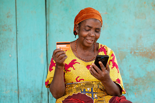 A cheerful elderly African woman holding her smartphone and credit card