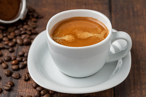 Image of frothy coffee americano on table. The lid of the cup is in the back