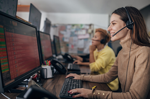 Two women, female taxi service operators with headsets working in call center on computers.