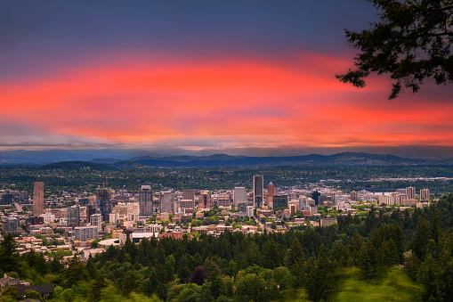 Colorful sunset over skyline of Portland, Oregon under heavy clouds photographed from Pittock Mansion viewpoint. Long exposure.