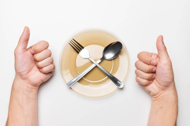 istock Male hands show a class gesture, a white table, an empty plate and a fork and a spoon lie on it, top view. delicious food idea 1466983677
