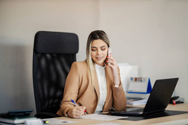 A secretary is sitting at the office and makes an appointment while talking on the phone with a client. stock photo