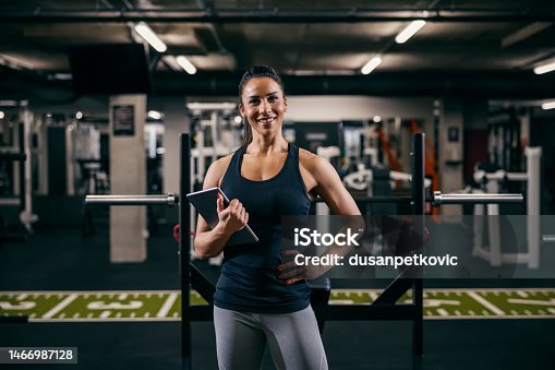 istock A female personal trainer is posing in a gym with tablet in her hands and smiling at the camera. 1466987128