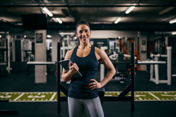 A female personal trainer is posing in a gym with tablet in her hands and smiling at the camera. stock photo