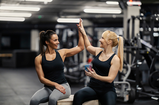 Two friends celebrating success in a gym. Achievement in a gym. Sportswomen giving high five to each other.